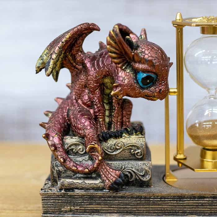 Ampulheta decorativa em bronze com escultura de bebê dragão vermelho detalhado abraçando a base de vidro.